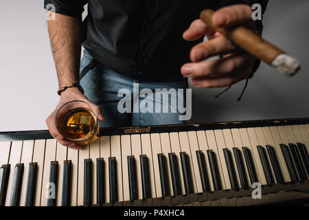 Cropped shot de l'homme assis en face de piano avec cigare et verre de whisky Banque D'Images