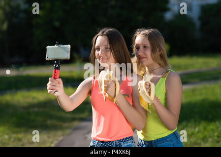 Deux jeunes filles amies d'écolière. L'été dans la nature. Dans ses mains est titulaire d'appareil photo. Mange des bananes. La notion de jeunes blogueurs. Manger émotionnel heureux sourire. Banque D'Images