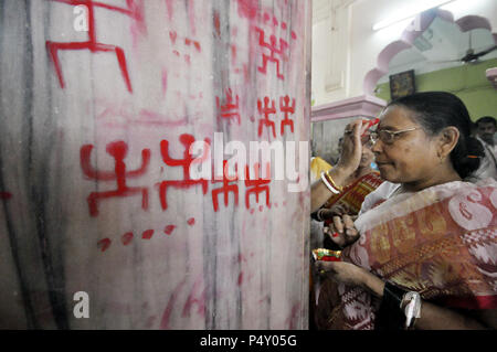 Une femme indienne appliquant vermillon sur son visage pendant le Ambubachi festival. Le swastika est une figure géométrique et une ancienne icône religieuse qui est tiré de vermillon sur le mur du temple dans le cadre des rituels d'Ambubachi à Agartala, capitale de l'Etat de Tripura, nord-est de l'Inde. Banque D'Images