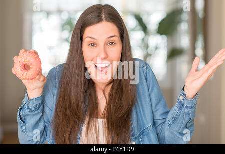 Hungry woman donut rose très heureux et excité, lauréat expression célébrant la victoire de crier avec grand sourire et mains levées Banque D'Images