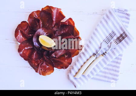 Tranches de viande italienne Bresaola servi avec de l'huile d'olive et de citron sur une plaque sur fond blanc. Entrées traditionnelles antipasti. Vue d'en haut. Banque D'Images