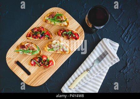 Brushetta définie pour le vin. Variété de petits sandwichs au jambon, tomates, roquette, basilic frais et sauce balsamique servi sur planche de bois avec gla Banque D'Images