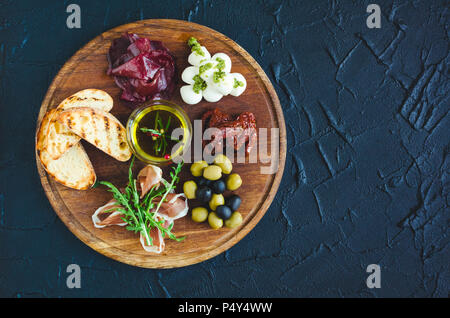 Assortiment de tapas espagnoles ou antipasti italiens : jambon prosciutto, bresaola, mozzarella, tomates séchées, olives et pain grillé sur planche de bois. Une nourriture Banque D'Images