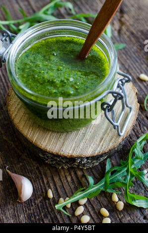 Pesto de roquette maison dans un bocal en verre avec les pignons de pin, roquette fraîche et l'ail sur la vieille table en bois rustique. Variante du pesto au basilic italien traditionnel Banque D'Images