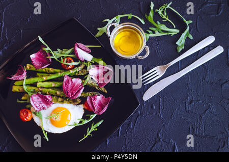 Œuf frit aux asperges, tomates cerise, de la chicorée et la roquette dans la plaque noire sur fond de pierre avec place pour le texte. Dîner santé concept. Deliciou Banque D'Images