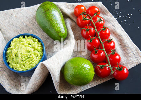 Conclussions traditionnelle sauce guacamole mexicain dans Bol en céramique et les ingrédients sur fond sombre. Ordinateur portable. Vue de côté. Banque D'Images