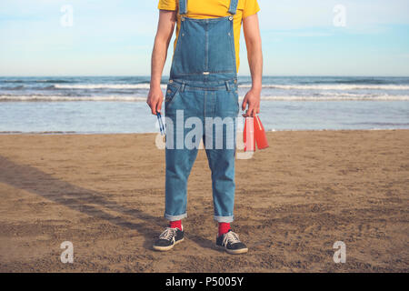 L'homme en salopette debout sur la plage de bouteilles de boissons sans alcool Banque D'Images