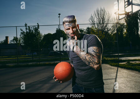 Portrait de jeune homme tatoué avec le basket-ball sur cour Banque D'Images