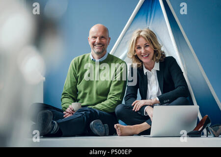 Happy businessman and businesswoman sitting at tipi à l'intérieur avec coffre Banque D'Images