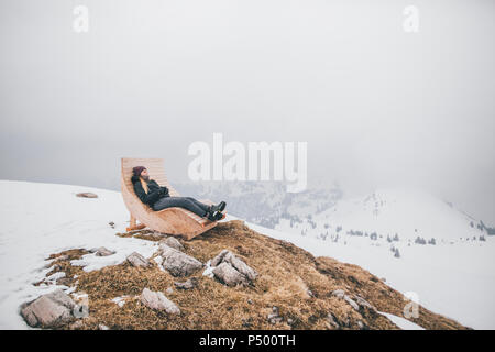 L'Autriche, de Kitzbuehel Kitzbühel Horn, jeune femme, de vous détendre sur une chaise longue en hiver looking at view Banque D'Images