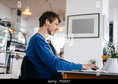 L'homme souriant dans un café avec écouteurs using laptop Banque D'Images