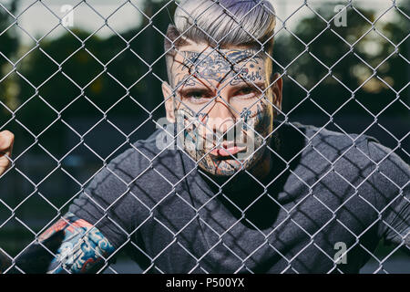 Portrait de jeune homme tatoué derrière fence Banque D'Images