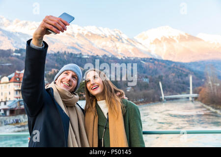 L'Autriche, Innsbruck, portrait of happy young couple with smartphone selfies en hiver Banque D'Images