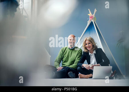 Smiling businessman and businesswoman sitting at tipi à l'intérieur avec coffre Banque D'Images