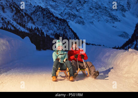 Heureux couple Sledding in snow-covered landscape at night Banque D'Images