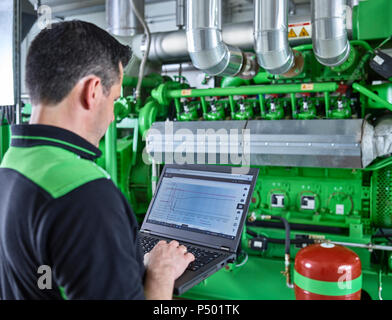 Production combinée de chaleur et d'électricité, worker using laptop in face de moteur à gaz Banque D'Images