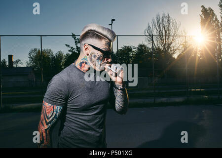 Jeune homme tatoué portant des lunettes fumer une cigarette Banque D'Images