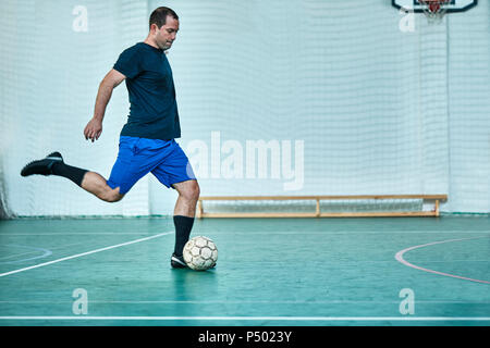 Homme jouant le tir de la balle de soccer intérieur Banque D'Images