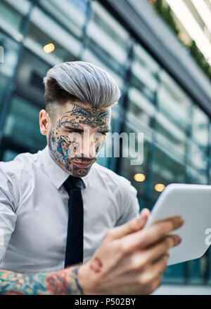 Jeune homme tatoué avec visage, using digital tablet Banque D'Images