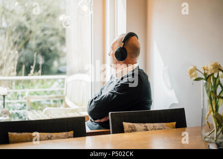 Senior man sitting at home, écouter de la musique, à la fenêtre de Banque D'Images