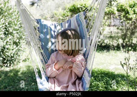 Petite fille assise sur le hamac dans le jardin Banque D'Images