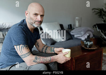 Tattooed man à la maison assis sur la table, boire du café Banque D'Images