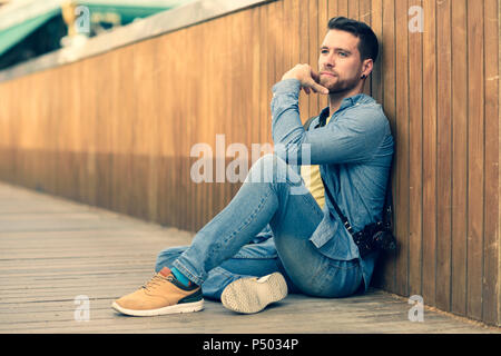 Jeune homme avec l'appareil photo assis sur la passerelle Banque D'Images