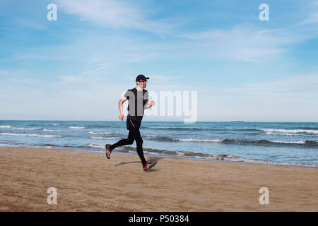 L'Espagne, l'homme vêtu de noir le jogging sur la plage Banque D'Images