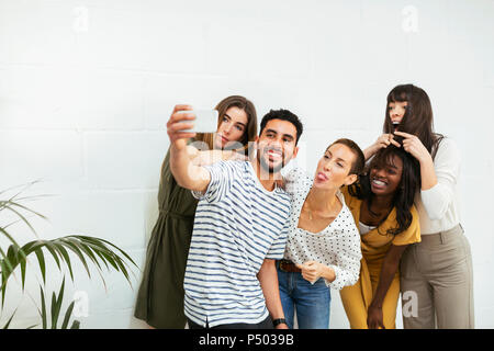 Collègues ludiques debout à mur de brique en tenant un selfies Banque D'Images