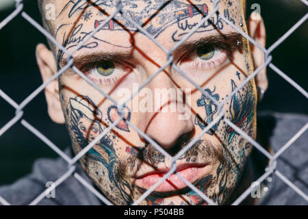 Visage de jeune homme tatoué derrière fence Banque D'Images