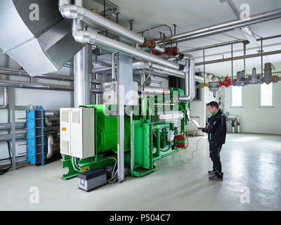 Production combinée de chaleur et d'électricité, worker using laptop in face de moteur à gaz Banque D'Images