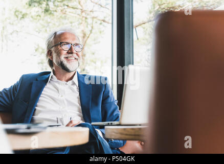 Smiling mature woman sitting at table in a cafe with laptop Banque D'Images