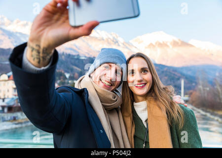 L'Autriche, Innsbruck, portrait of happy young couple with smartphone selfies en hiver Banque D'Images