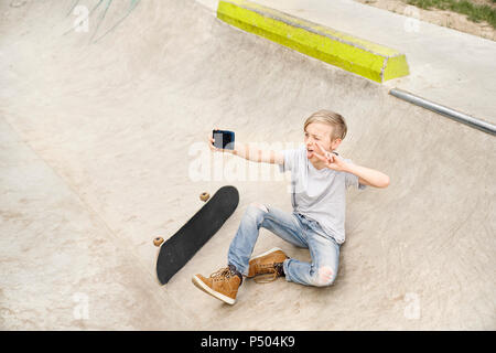 Garçon avec skateboard en tenant vos autoportraits avec smartphone Banque D'Images