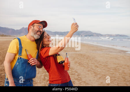 Couple avec des boissons non alcoolisées en tenant avec smartphone selfies sur la plage Banque D'Images