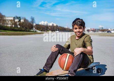 Portrait of smiling boy with longboard et de basket-ball extérieur Banque D'Images