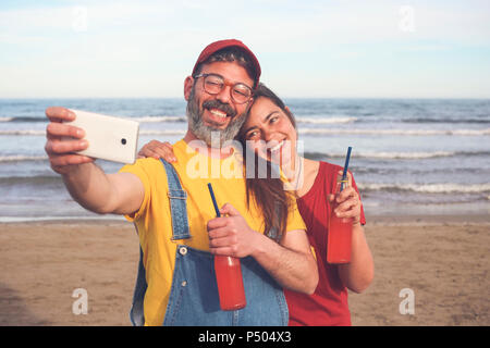Couple avec des boissons non alcoolisées en tenant avec smartphone selfies sur la plage Banque D'Images