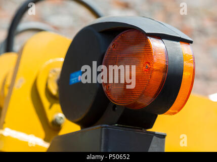 Feu orange d'avertissement jaune de la road machinery close-up sur fond flou de ses mécanismes, les flexibles hydrauliques et mur de brique Banque D'Images