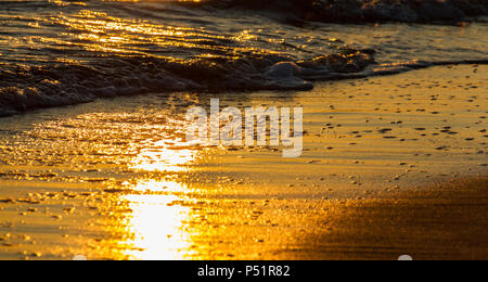 Belles formes colorés créés par les vagues sur une plage de sable et de réflexions soleil au coucher du soleil Banque D'Images