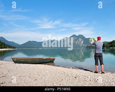 Photographe avec oeil au viseur est taking photo du lac avec des montagnes des Alpes en arrière-plan. Les œuvres d'artistes. Banque D'Images