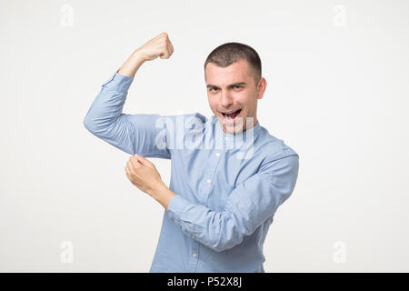 Bel homme d'âge moyen en chemise bleue pointant biceps exprimant force et vie saine. Il est fort et fuul de l'énergie Banque D'Images