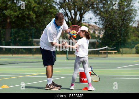 Session d'entraînement de tennis pour enfants / leçon ayant lieu sur un court de tennis avec les enfants / kids et entraîneur de tennis professionnel, en été. UK. (99) Banque D'Images