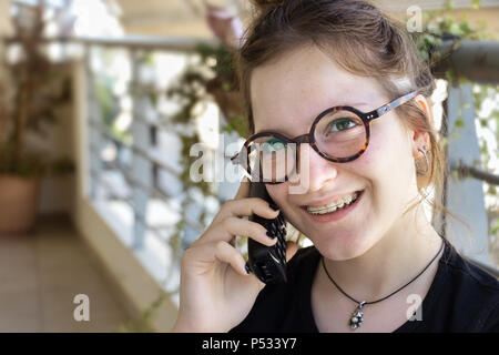 Un adolescent girl orthodontie accolades est parlé par téléphone à la maison portant des lunettes. Banque D'Images