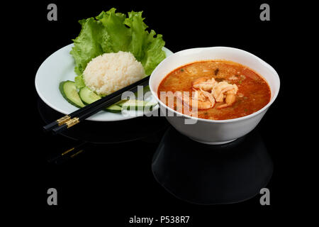 Tom Yum ou tom yam est un type de soupe Thaï aigre et piquante, généralement cuite avec des crevettes. Servi avec du riz et baguettes. Isolé sur bac réfléchissant noir Banque D'Images