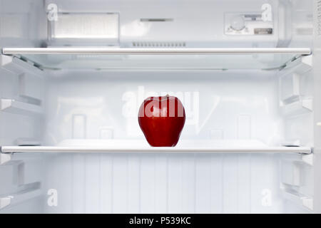 Le dirigeant d'une pomme rouge sur une étagère dans un réfrigérateur vide. Une pomme fraîche dans un réfrigérateur propre vide. Fruits est un refroidissement dans le stockage. Banque D'Images