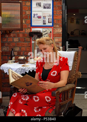 1940 Une dame enthusiast détend la lecture d'un livre vintage dans une reconstitution d'un 1940 cuisine au week-end du patrimoine Burscough. Banque D'Images