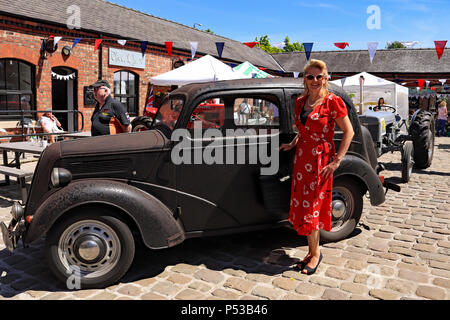 Une dame habillée d'une robe rouge de style des années 1940 se trouve à côté de sa vieille Ford voiture sauvé d'un garage où il était de 41 ans. Banque D'Images