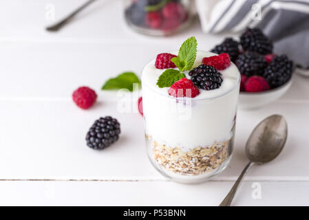 Yaourt blanc avec du muesli et des framboises dans un bol en verre blanc sur fond de bois. Banque D'Images