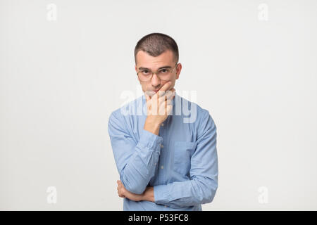 Jeune homme en chemise bleu désorienté permanent abasourdi isolé sur fond de mur gris. Concept de prise de décision. Les droits de l'expression faciale des émotions Banque D'Images