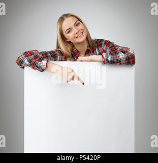 Young Smiling adolescent blond girl blanc Tenez le papier blanc et montre sur elle. Isolé sur fond blanc. Banque D'Images